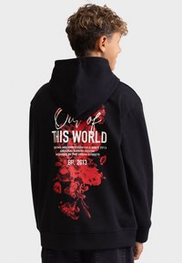 Felpa nera con grafica floreale rossa sul retro, con testo bianco. Il materiale sembra morbido; il design include un grande cappuccio e polsini a coste.