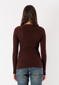 Maglietta marrone a maniche lunghe con scollo a barca, silhouette aderente e tessuto testurizzato, abbinata a jeans di denim azzurri.