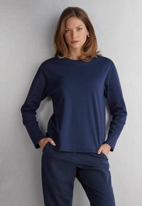 Marineblaue Langarmbluse aus einem glatten, elastischen Material mit Rundhalsausschnitt und lockerer Passform. Kombiniert mit passenden marineblauen Hosen.