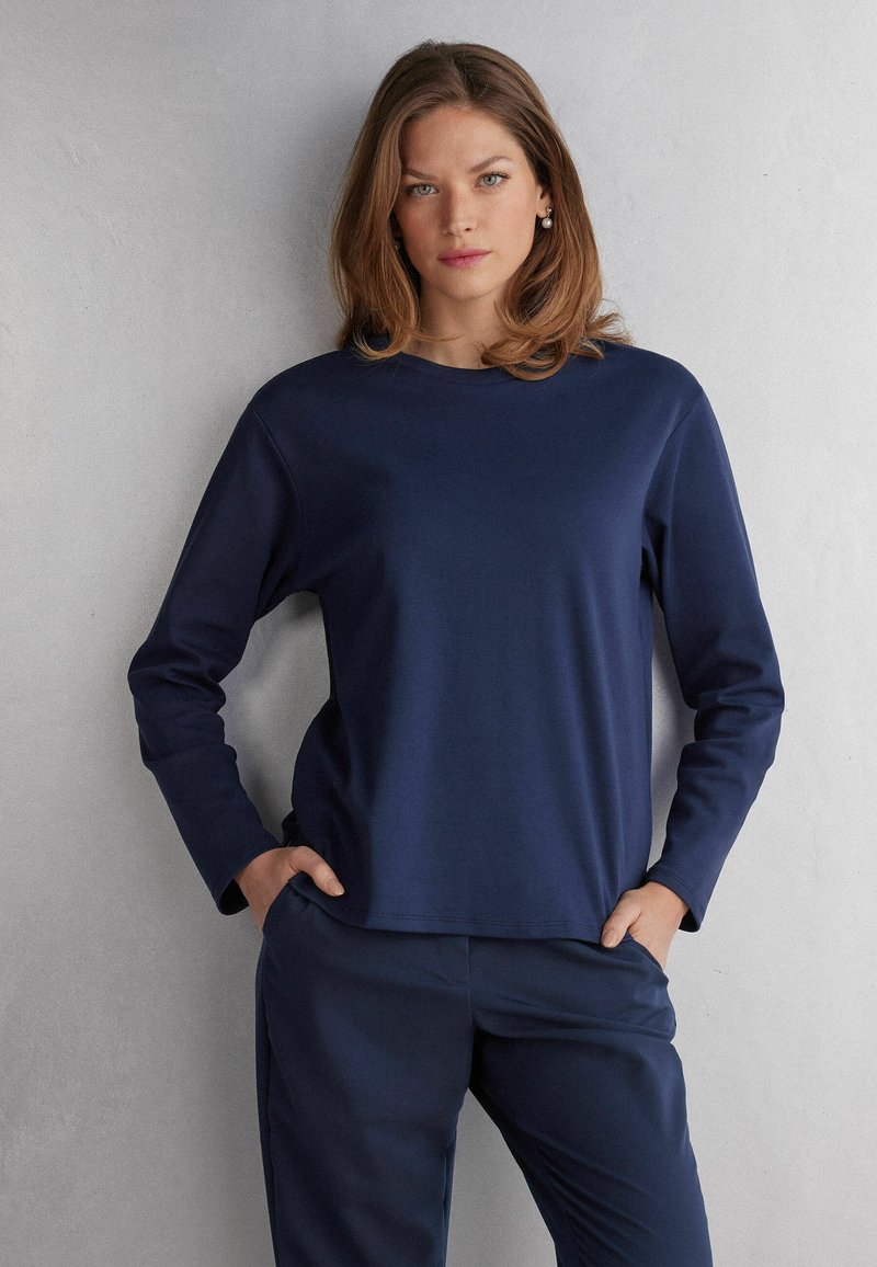 Marineblaue Langarmbluse aus einem glatten, elastischen Material mit Rundhalsausschnitt und lockerer Passform. Kombiniert mit passenden marineblauen Hosen.