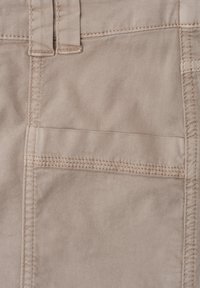 Gros plan d'une poche en tissu beige avec double couture horizontale et passants de ceinture sur un pantalon ou short décontracté.