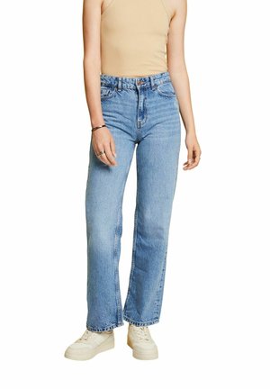 Jean taille haute bleu clair avec une coupe droite, un léger délavage et un style à cinq poches, associés à des baskets blanches.