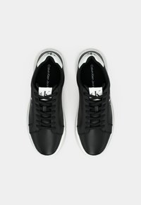 Een paar zwart-witte Calvin Klein Jeans sneakers met zwarte veters, van bovenaf bekeken op een effen witte achtergrond.