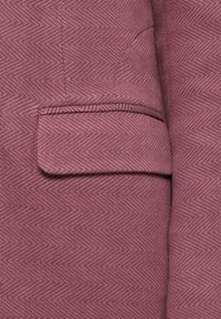 Ύφασμα σκούρου ροζ σακακιού με σχέδιο ψαροκόκκαλο, που διαθέτει μία εξωτερική τσέπη στο στήθος και έχει ομαλή, υφή με υφή.