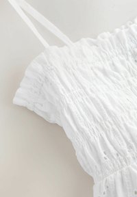 Witte, mouwloze top met een smockontwerp, voorzien van delicate kantdetails en een textuurstof. Dunne banden maken het ontwerp compleet.
