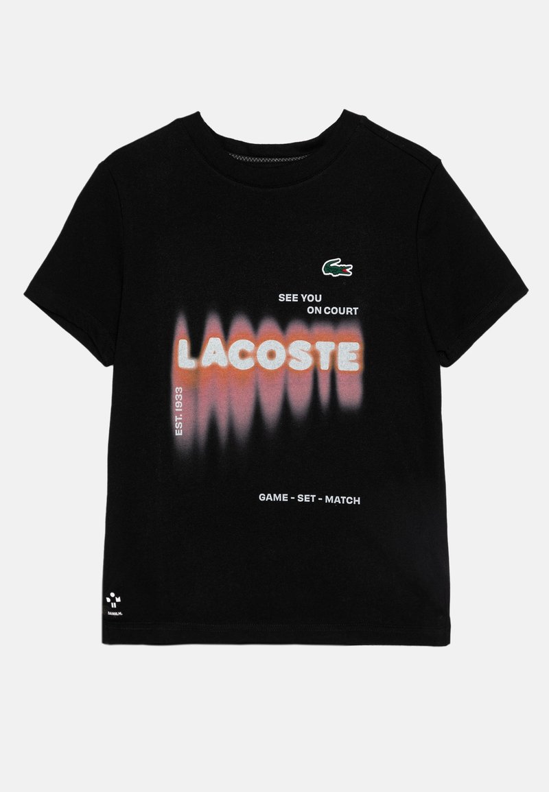 T-shirt nera in cotone con design testuale a gradiente con la parola "LACOSTE" in arancione e bianco, accompagnata da slogan e dal logo del coccodrillo.