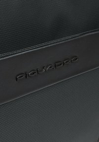 Zaino nero con corpo in nylon testurizzato, caratterizzato da un dettaglio liscio in pelle nera. Logo "Piquadro" in rilievo ben evidente.