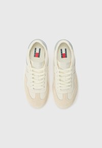 White and cream sneakers with suede accents, featuring a textured design, flat laces, and a branded tag in red, white, and blue.