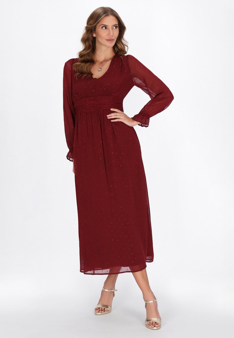 Rochie maxi burgundy cu mâneci lungi, decolteu în V, talie strânsă, material transparent și detalii subtile. Asortată cu sandale metalice cu bareta la gleznă.
