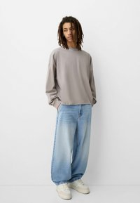 Siv, dolg rokav pulover s sproščenim krojem, v kombinaciji s svetlo modrimi širokima hlačami. Bele športne copate dopolnjujejo izdelek.