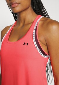 Roze sportieve tanktop met een ronde halslijn, voorzien van contrasterende schouderbanden met 'Under Armour' branding en een klein logo op de borst.