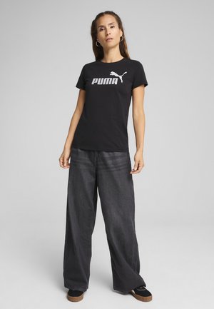 Čierne bavlnené tričko s bielym logom "PUMA", skombinované s voľnými tmavými džínami a čiernymi topánkami s textúrovanou podrážkou.