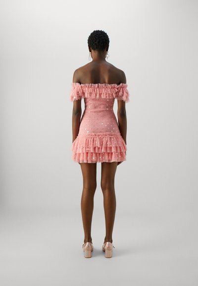 Rožinė off-the-shoulder suknelė su bumelės rankovėmis, daugiapakopė kraštinė puošti blizgučiais. Dėvima su skaidriais aukštakulniais batais.