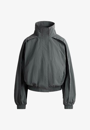 Jachetă ușoară de culoare gri închis cu guler înalt, mâneci lungi, manșete elastice și talie elastică, prezentată pe un fundal alb simplu.