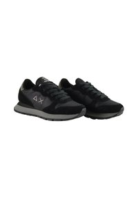 Un paio di sneaker nere con lacci e suole grigie, logo discreto sui lati e colli imbottiti, angolati leggermente verso destra su uno sfondo bianco.