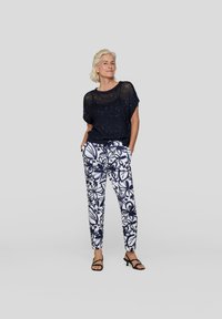 Navy knitted top with short sleeves, paired with white trousers featuring a blue floral pattern, complemented by black strappy sandals.