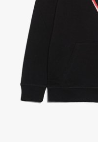 Sweatshirt en coton noir avec une poche avant, des poignets côtelés et une texture lisse. Présente un design graphique diagonal rouge et blanc.