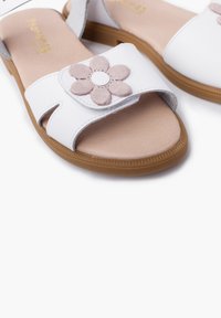 White leather sandals with a brown sole, featuring a pink fabric flower accent on the strap and an open toe design.