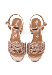 Sandali con tacco bloccato in oro rosa metallico presentano un cinturino decorativo con motivo a intaglio e chiusura con fibbia. Superficie liscia e lucida.