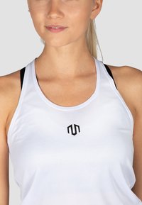 Valge sportlik tank top ümarate kaelus, millel on keskel must logo ja õlgadel nähtavad mustad rihmad.