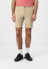 Beige shorts with rolled cuffs, made of cotton blend fabric. Worn with black sneakers and white socks. Styled with a red t-shirt.