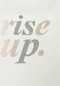 Weißer Stoff mit dem Text "rise up" in verschiedenen farbigen Strasssteinen: schwarz, gold und roségold, mit einem Punktakzent.