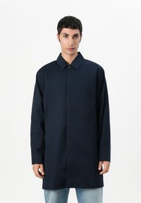 Casaco azul marinho feito de um tecido suave; possui colarinho, fecho frontal com botões e bolsos laterais; corte descontraído com mangas longas.