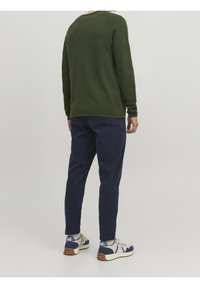 Grön tröja med långa ärmar, rundad nederkant, tillsammans med marinblå slim-fit byxor. Avslappnade sneakers med blå och krämfärgade accenter fulländar outfiten.