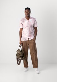 Camicetta a maniche corte con strisce verticali rosa e bianche, abbinata a pantaloni larghi marroni e una borsa verde con dettagli scuri. Sneakers bianche.