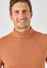 Roodbruin coltrui met ribbelstructuur. De stof is zacht en aansluitend, met een hoge kraag en een naadloos ontwerp.