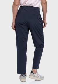 Marineblaue, tapered Hosen aus leichtem Stoff mit glatter Textur und einer einzelnen Gesäßtasche. Kombiniert mit mehrfarbigen Sneakers.