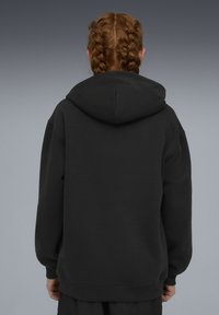 Sweat à capuche noir avec une grande capuche, des manches longues et des poignets côtelés. Fabriqué dans un matériau doux, présentant un design simple et minimaliste.