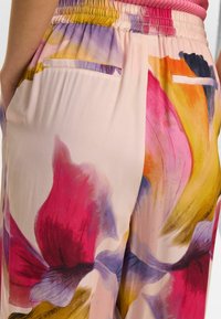 Pantaloni leggeri con motivo floreale in tonalità pastello di rosa, viola e arancione, dotati di vita elasticizzata e tasche laterali.