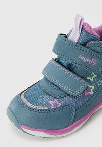 Niebieskie dziecięce sneakersy z zapięciami na rzep, wykonane z siateczkowego materiału, z wzorami gwiazdek w różowym i żółtym kolorze oraz fioletowymi akcentami na podeszwie i pięcie.