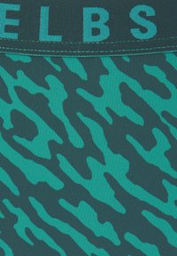 Turkoosi uimaportit, joissa on musta abstrakti kuvio, leveällä joustavalla vyötäröosalla, jossa on brändin nimi kontrastivärisin teal-värisin kirjaimin.