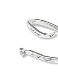 Bracelet en métal argenté au design lisse et courbé ; présente une marque gravée indiquant "05". Surface polie distincte avec une épaisseur variable.