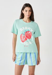 Maglietta in cotone verde menta con stampa "BERRY SPECIAL" e due fragole rosse. Abbinata a pantaloni corti a strisce verde chiaro e blu.