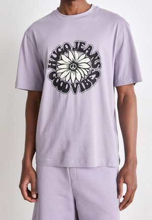 Lichtpaarse katoenen t-shirt met een centraal grafisch ontwerp van een bloemenmotief met een vredesteken en de vetgedrukte tekst "HUGO JEANS GOOD VIBES" eronder.