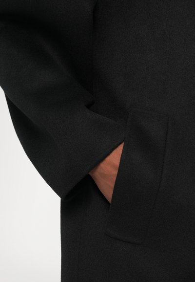 Palton negru din lână, cu un design elegant, buzunar mare și textură fină. Aspect minimalist, cu o finisare curată și detalii subtile.