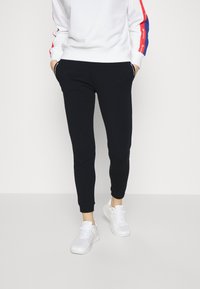 Svarta joggingsbyxor med slim fit, tillverkade av mjukt tyg, med sidofickor och ribbade muddar, ihop med vita träningsskor.