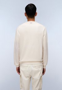 Sudadera beige claro con cuello y puños de canalé, que presenta un pequeño diseño en la parte posterior del cuello. Combinada con pantalones cargo crema.