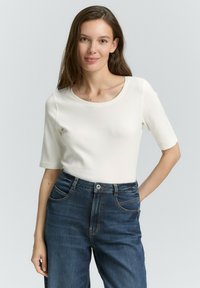 Witte, ronde hals top met korte mouwen, aansluitend design, gecombineerd met donkerblauwe denim high-waist jeans met zichtbare stiksels en zakken.