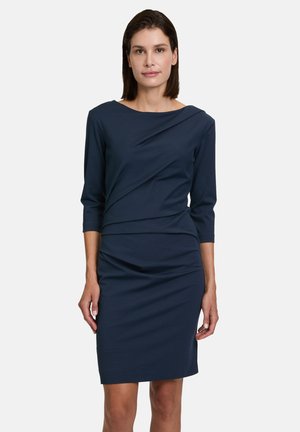 Marineblauwe jurk met driekwartmouwen, gedrapeerd ontwerp op de bovenkant en een strakke pasvorm die boven de knie eindigt. Glad stoftextuur.