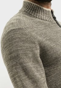 Maglione grigio con un motivo a maglia testurizzata e colletto a coste, con cerniera frontale. Il tessuto sembra morbido e caldo con un design aderente.
