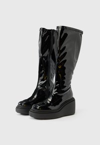 Crne, visoke čizme od lakirane kože do koljena s klinastom petom. Imaju elegantan dizajn, šiljati vrh i bočni zatvarač za lako obuvanje.