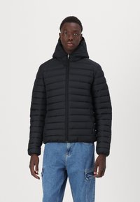 Veste coupe-vent noire avec fermeture éclair à l'avant, capuche et poignets côtelés. La veste a un design matelassé et est associée à un jean bleu clair.