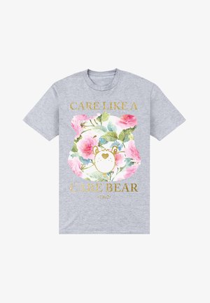 Grå T-shirt med et blomster-ansigt af en bamse og guldfarvet tekst "Care like a Care Bear 1982" på fronten.