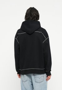 Sort hættet sweatshirt med kontrasterende grå syninger, afslappet pasform og kængurulomme. Blødt materiale med ribkantede ærmer og nederkant.