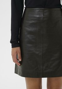 Crna kožna mini suknja s glatkom teksturom, ravnim krojem i suptilnim sjajem. Detalj šivanja duž srednjeg šava na leđima.