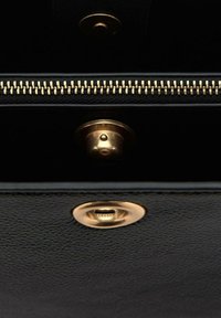 Interno di una borsa a mano in pelle nera con una cerniera dorata, chiusura a scatto in ottone e rivestimento in tessuto testurizzato.